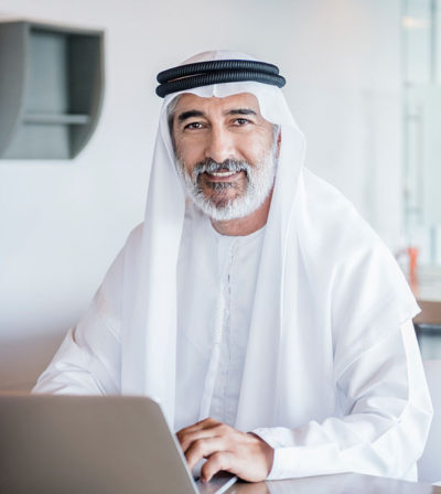 Businessman working in office with laptop computer wearing traditional Arabian agal and ghoutra.